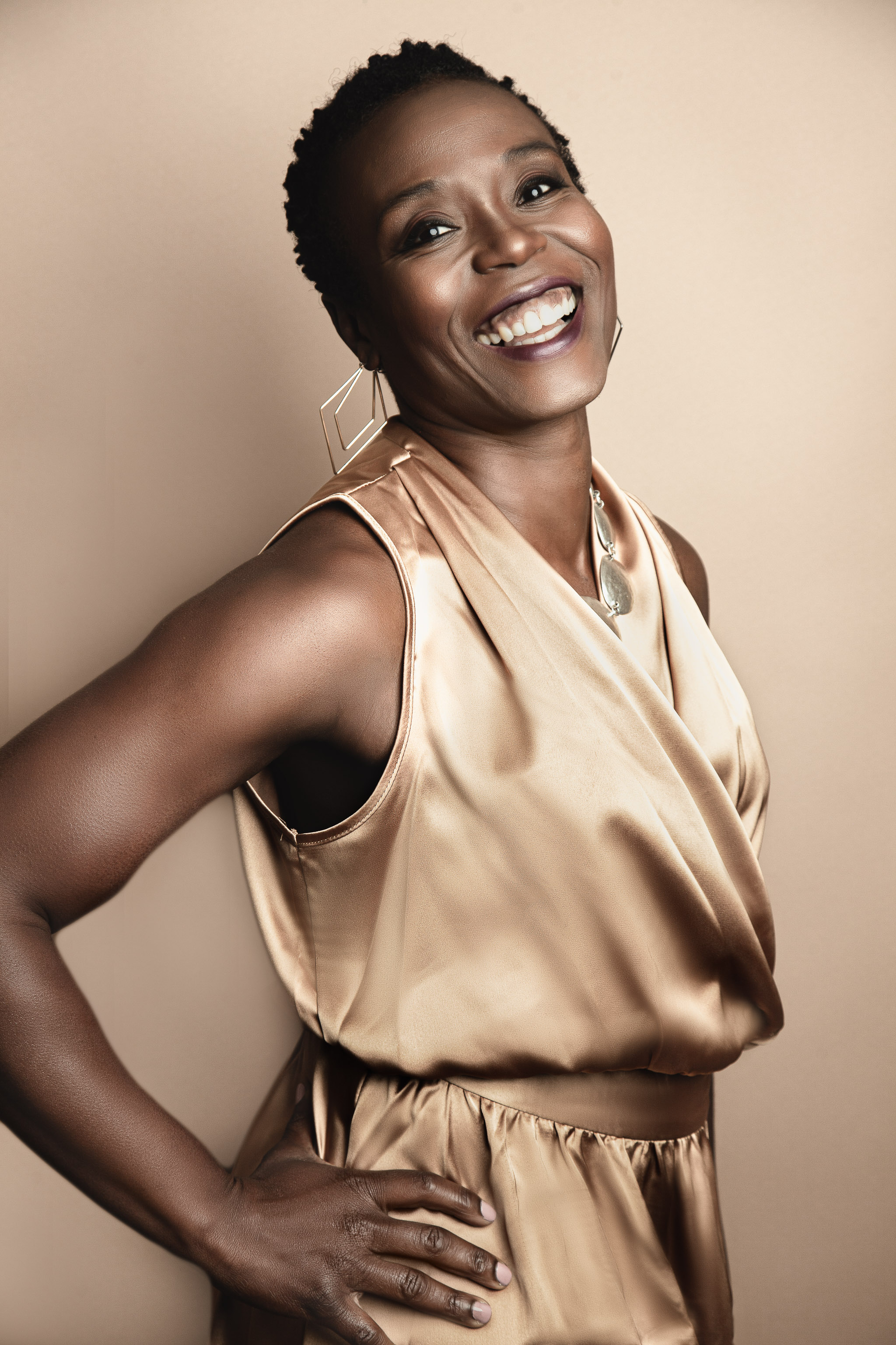 black 40 year old woman dressed in gold dress smiling happily at the camera laughter