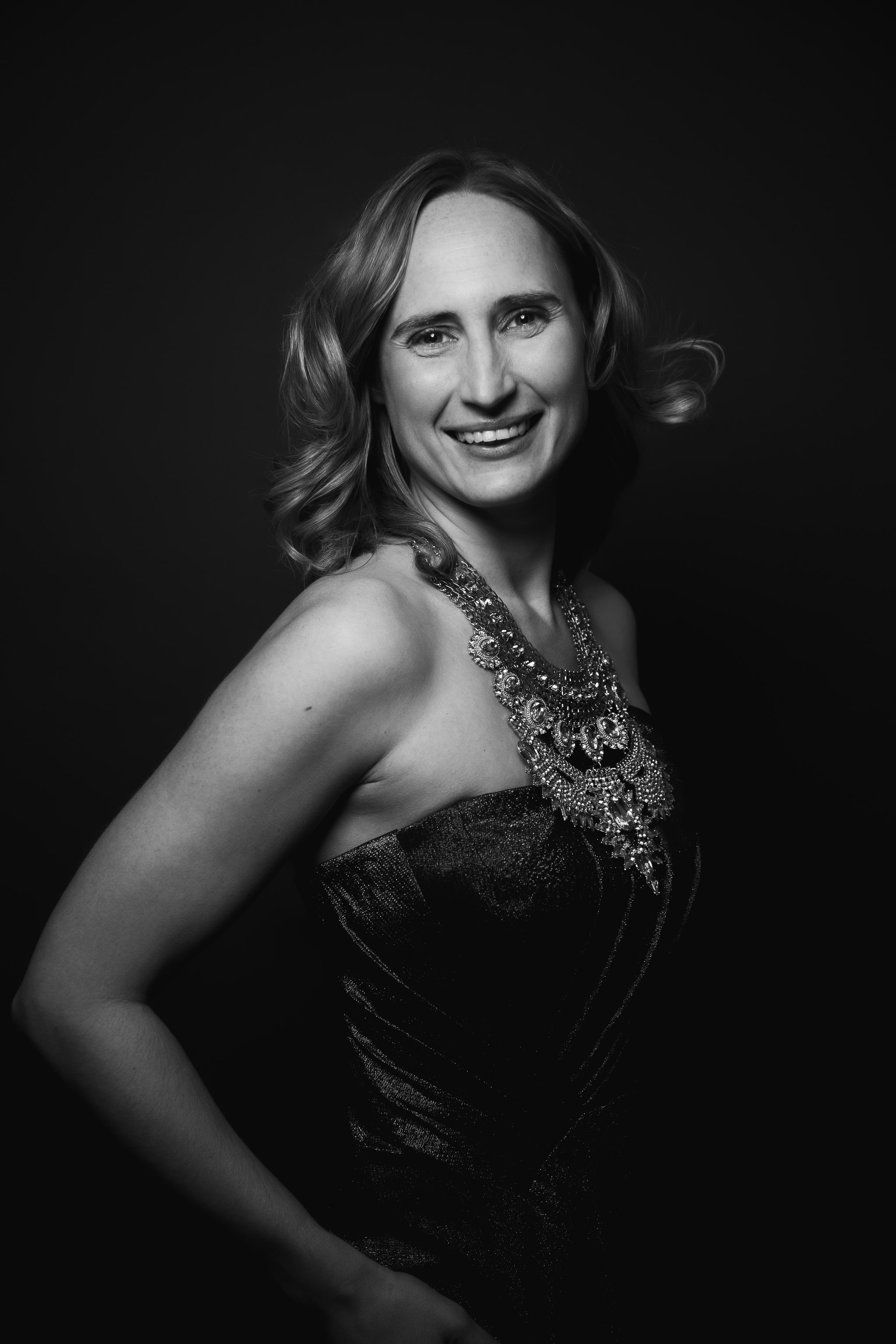 long island mom short hair smiling in front of the camera wearing oversized crystal necklace in a strapless dress