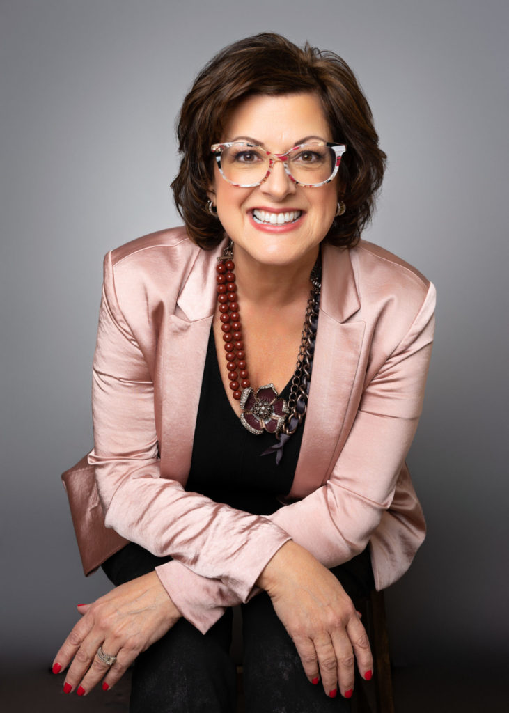 Professional headshot of a real estate agent female smiling in a pink satin blazer and statement necklace, photographed in Farmingdale on Long Island for a personal branding photoshoot