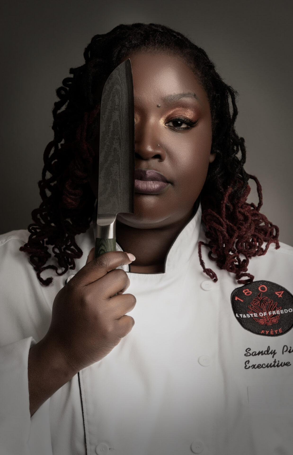 Dramatic studio portrait of a Black woman chef with knife in hand, conveying emotion and intensity