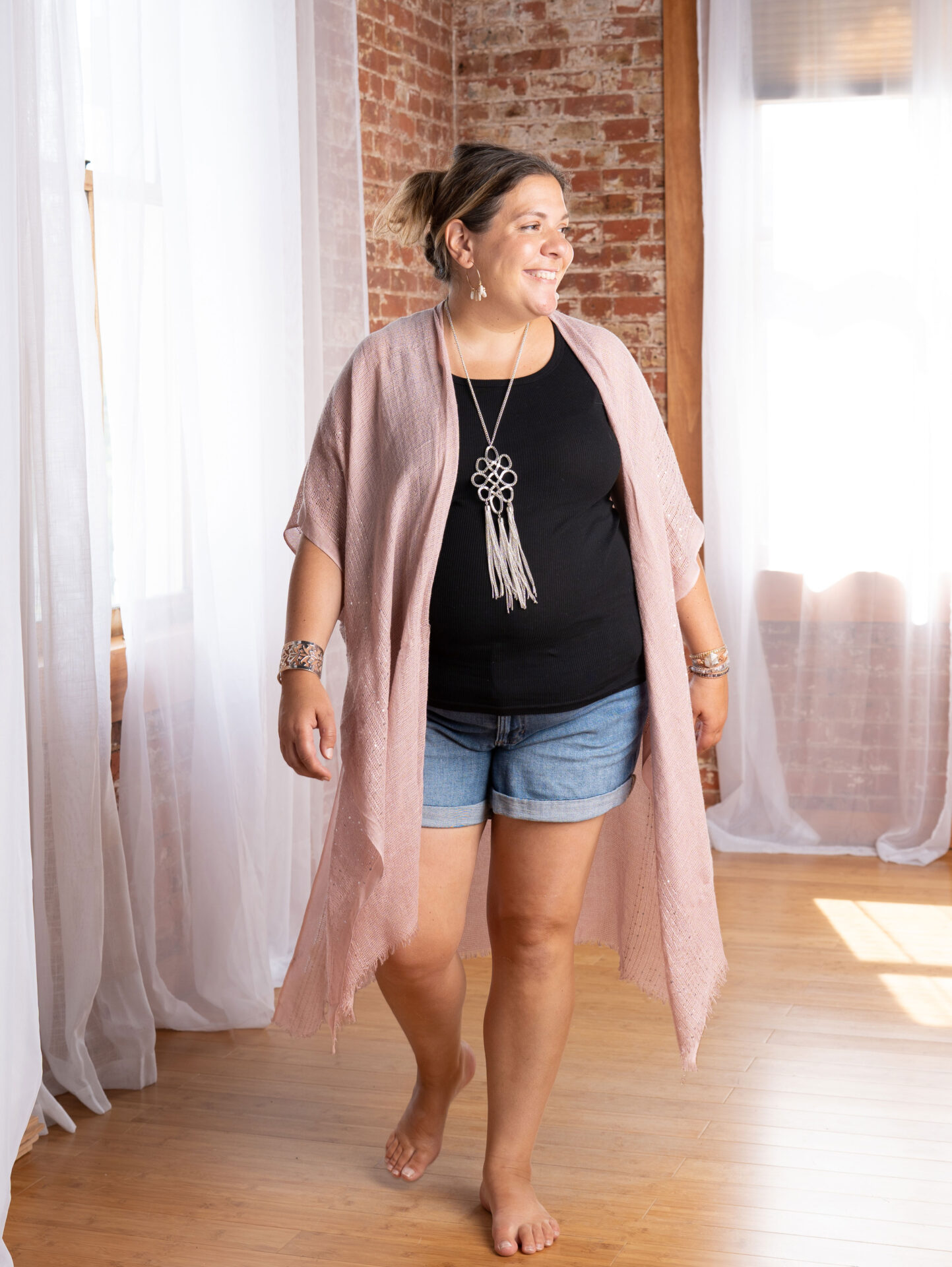 Personal branding portrait of a woman smiling and walking barefoot in a bright studio with exposed brick walls, photographed at The BeVard Studio in long island, NY.