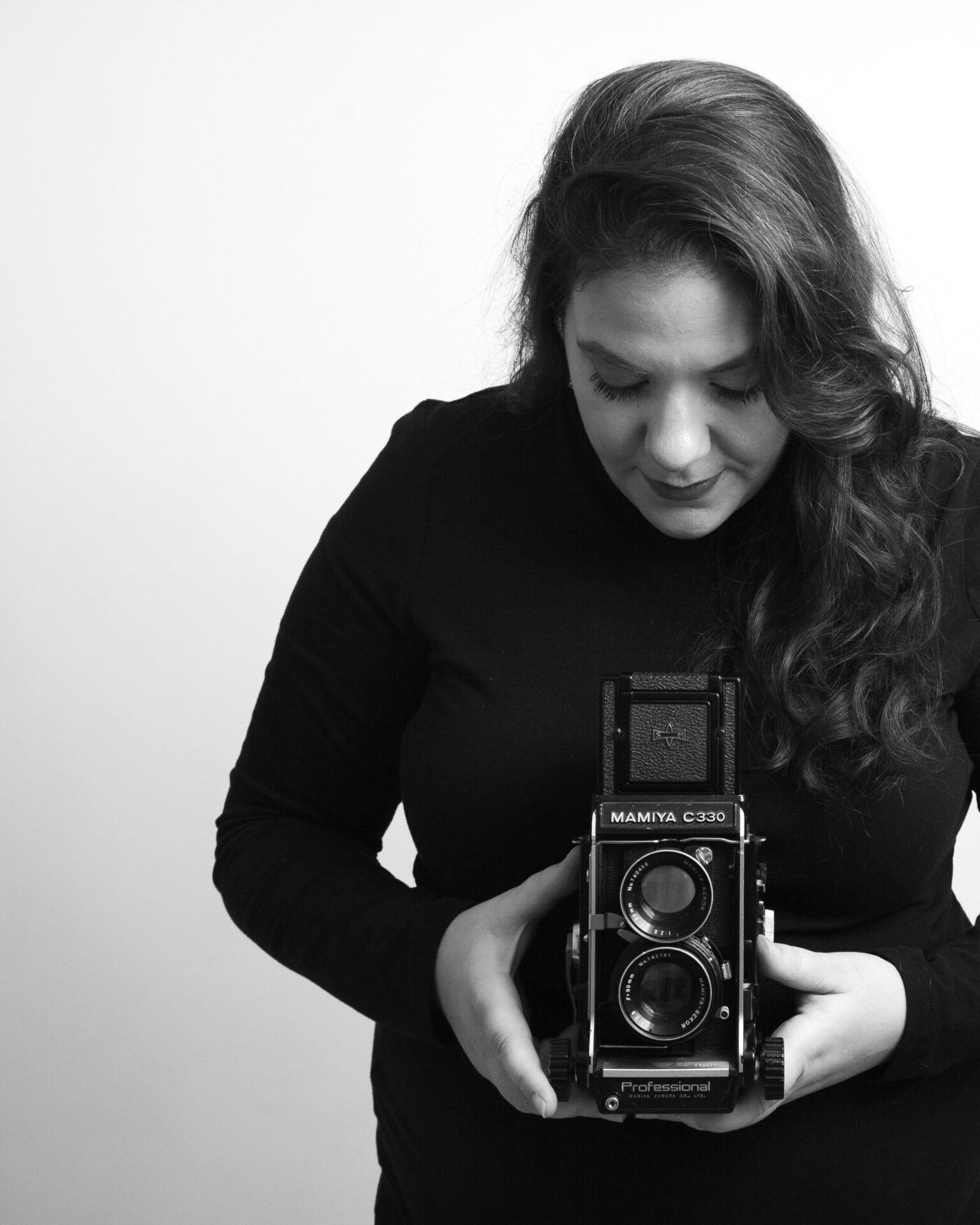 black and white vintage style woman holding a medium format camera looking down and taking a photo