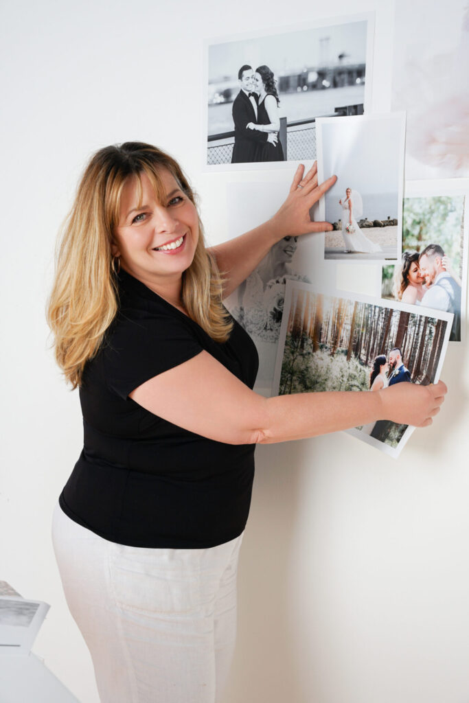 Photographer smiling while arranging printed wedding portraits on a studio wall.