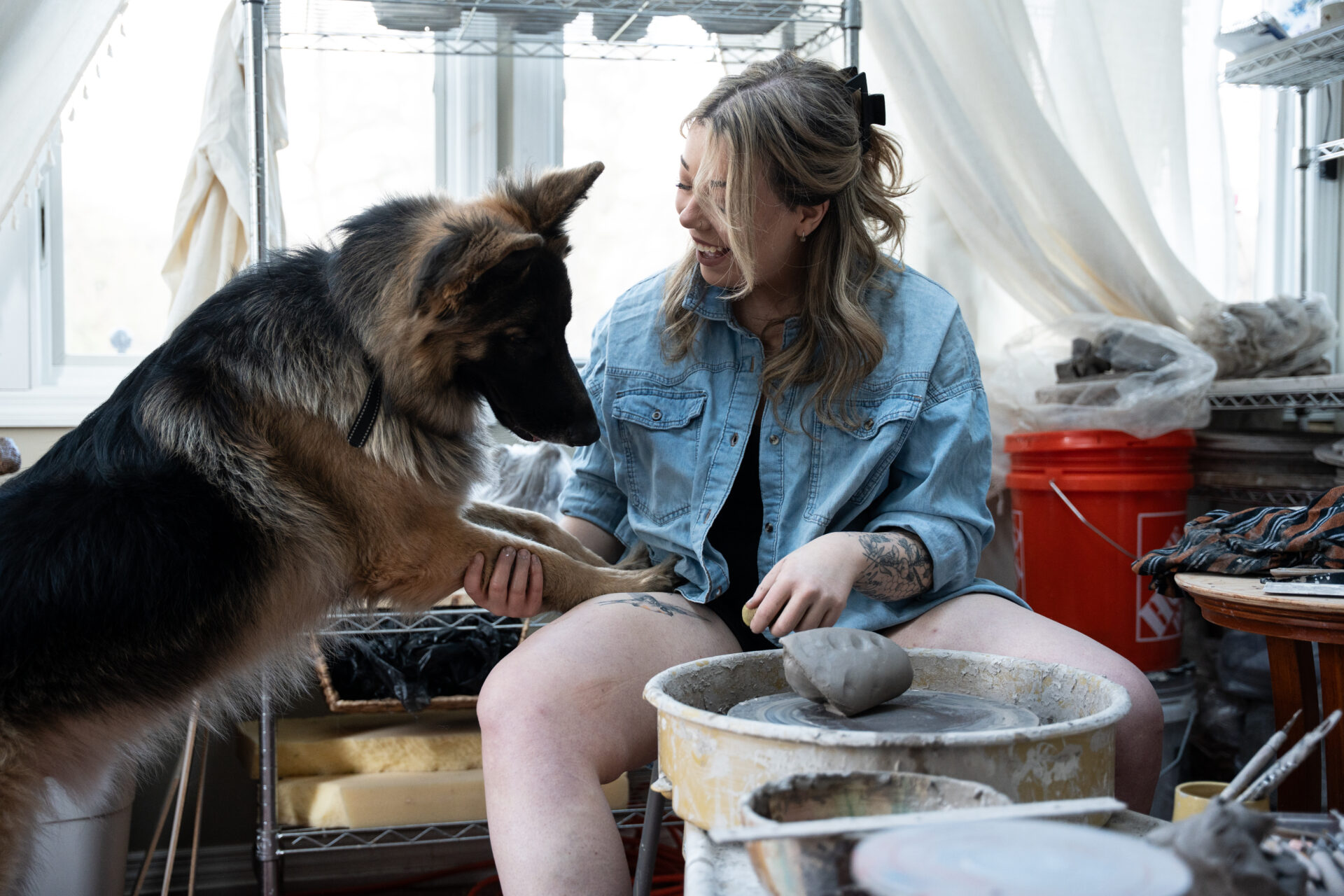 personal branding of pottery artist sitting at her pottery wheen shaking her german shepherds dog paw